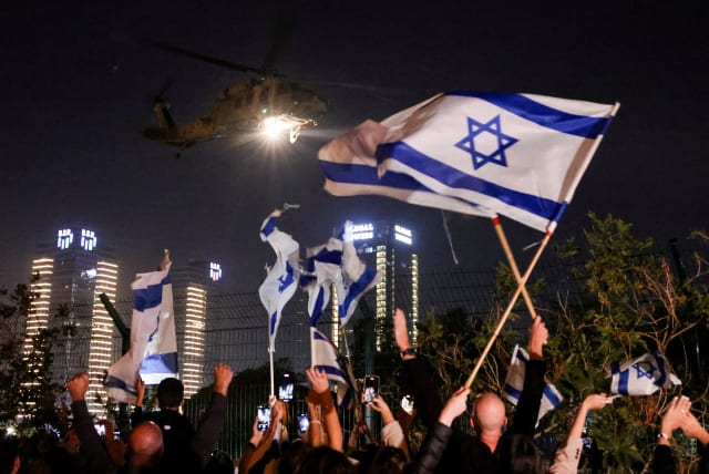 People wave Israeli flags as a helicopter, carrying hostages, departs from Schneider Children's Medical Center in Petah Tikva, Israel, November 24, 2023 (photo credit: RONEN ZVULUN/REUTERS)