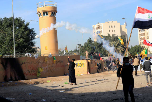 Protesters and militia fighters throw back a tear gas canister used by U.S. Embassy security men during a protest to condemn air strikes on bases belonging to Hashd al-Shaabi (paramilitary forces), outside the embassy in Baghdad, Iraq January 1, 2020. (photo credit: THAIER AL-SUDANI/REUTERS)
