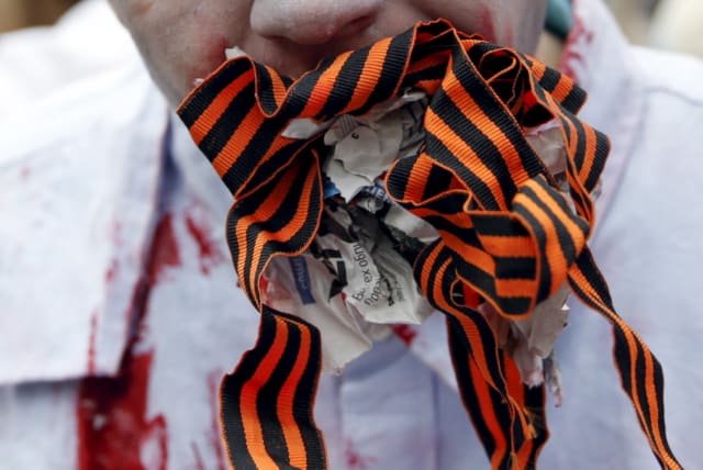 A participant dressed as a zombie holds pieces of a newspaper and St. George's Ribbons in his mouth during a performance to protest against the work of some local media, which they say promote and popularize Russian subversive propaganda in Ukraine, in Kiev, Ukraine, June 21, 2015. The St. George's  (photo credit: VALENTYN OGIRENKO/REUTERS)