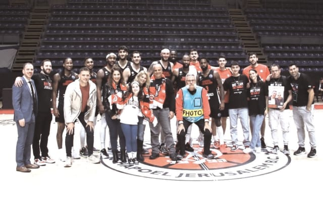  HAPOEL JERUSALEM players and management pose on the Pionir Arena court in Belgrade with a group of fans – including released hostage Ofir Engel and his family – who were flown in for the Reds’ 71-61 Champions League win over PAOK.  (photo credit: COURTESY HAPOEL JERUSALEM)