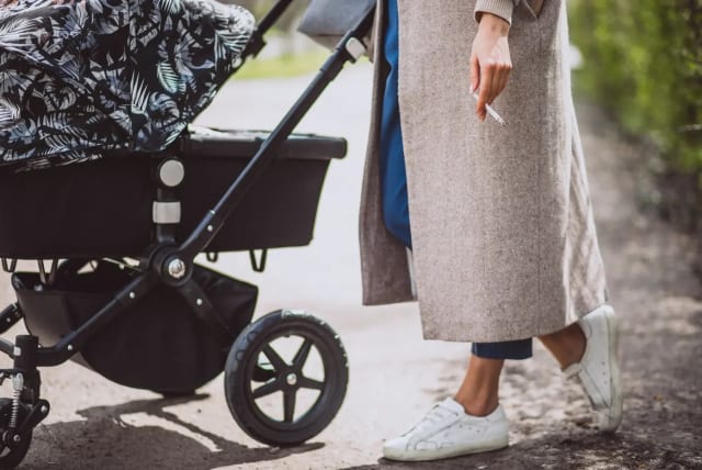 A young mother with a cigarette and a baby stroller (photo credit: SHUTTERSTOCK)