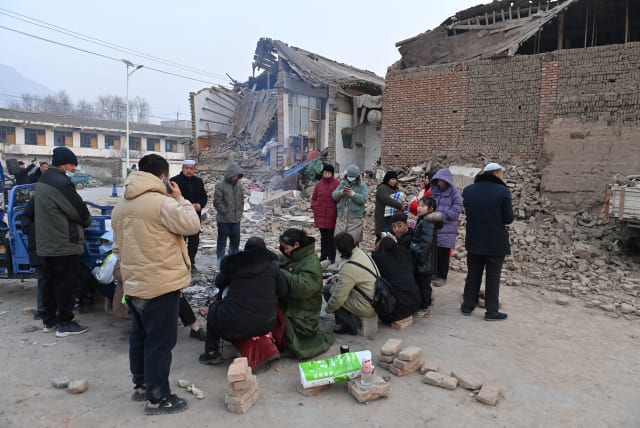  Residents keep warm by a fire next to damaged buildings at Dahejia town following the earthquake in Jishishan county, Gansu province, China December 19, 2023. (photo credit: CNSPHOTO VIA REUTERS)