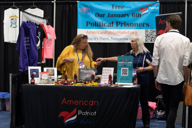  People stand at the table for American Patriot Relief, in front of a sign that reads Free Our January 6th Political Prisoners, as conservative leaders and personalities attend Turning Point USA's AmericaFest 2023 in Phoenix, Arizona, US December 16, 2023.  (photo credit: REUTERS/Caitlin O’Hara)