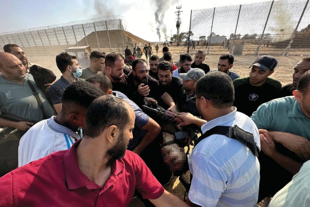  A REUTERS photo taken by Abu Mostafa on Oct. 7: Palestinians carry the body of an Israeli soldier slaughtered by Hamas after being pulled from a tank. (photo credit: Mohammed Fayq Abu Mostafa/Reuters)