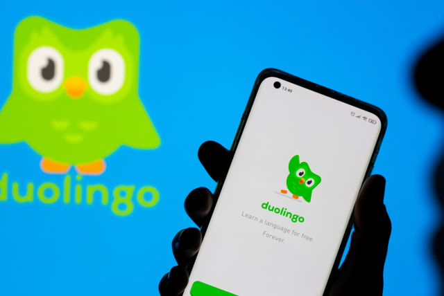 Woman with her smartphone poses in front of displayed Duolingo logo in this illustration taken, June 29, 2021.  (photo credit: DADO RUVIC/REUTERS)