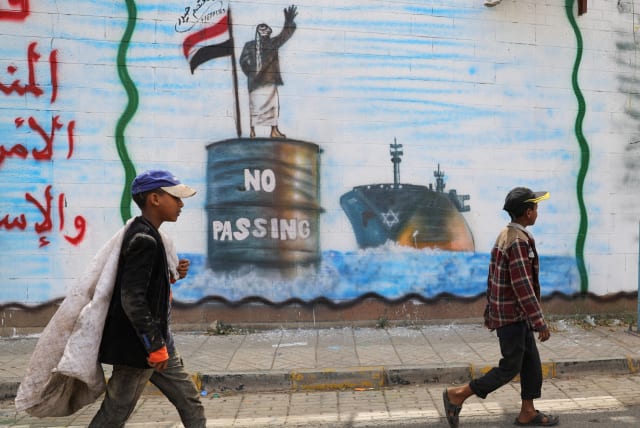  People walk past a graffiti, depicting a Houthi fighter stopping an Israeli ship off the coast of Yemen, painted on a wall of the Saudi embassy in Sanaa, Yemen February 15, 2024 (photo credit: REUTERS/KHALED ABDULLAH)