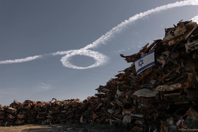  ‘RIBBONS OF Return,’ 2024. A warplane streaks across the sky above a graveyard of cars, remnants of the massacre. The plane crafts a ‘Bring them home’ ribbon in the sky.  (photo credit: CHEN SCHIMMEL)