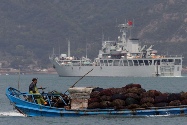 A fishing boat sails past a Chinese warship during a military drill off the Chinese coast near Fuzhou, Fujian Province, across from the Taiwan-controlled Matsu Islands, China, April 11, 2023. (photo credit: THOMAS PETER/REUTERS)