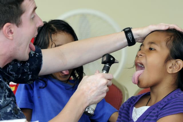A US Navy doctor checks a patient's tonsils during a Pacific Partnership 2010 medical civic action project. (photo credit: PUBLIC DOMAIN)