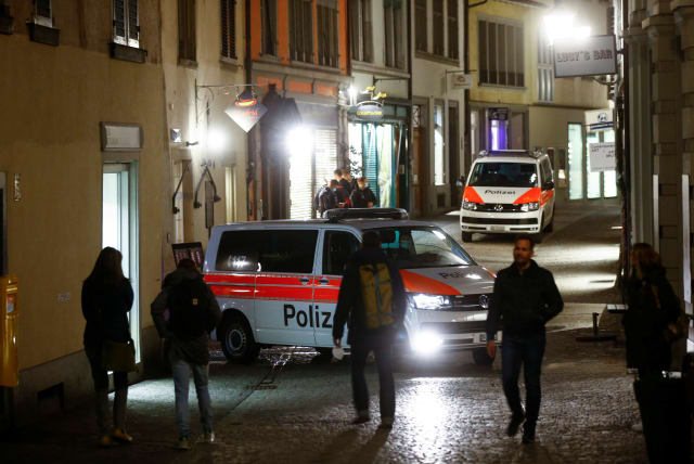  People walk past as Swiss police vehicles stand by to prevent expected illegal gatherings amid restrictions due to the coronavirus (COVID-19) pandemic, in the old town of Zurich, Switzerland, April 9, 2021. (photo credit: Arnd Wiegmann/Reuters)