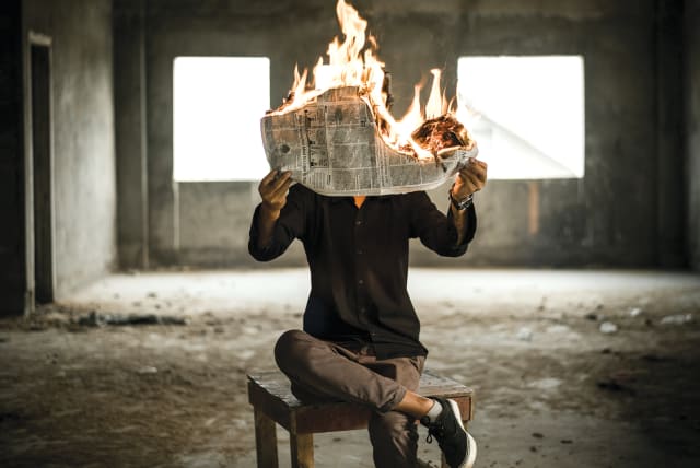  An illustrative image of a man holding a newspaper on fire. (photo credit: NIJWAM SWAGIARY/UNSPLASH)