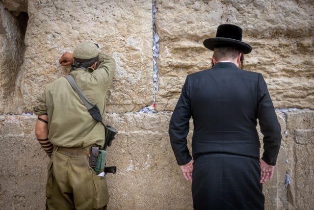  An Israeli soldier prays next to an ultra orthodox Jewish man at the Western Wall, in Jerusalem (photo credit: Chaim Goldberg/Flash90)