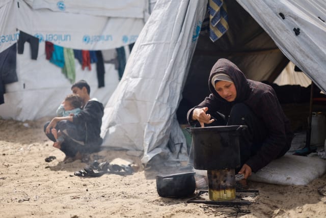  A woman cooks, as displaced Palestinians, who fled their houses due to Israeli strikes shelter in a tent camp, amid the ongoing conflict between Israel and the Palestinian Islamist group Hamas, in Rafah in the southern Gaza Strip, March 6, 2024. (photo credit: REUTERS/MOHAMMED SALEM)