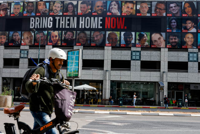  A man pushes a bike near a billboard with pictures of hostages kidnapped in the deadly October 7 attack on Israel by the Palestinian Islamist group Hamas from Gaza, in Tel Aviv, Israel March 18, 2024.  (photo credit: CARLOS GARCIA RAWLINS/REUTERS)