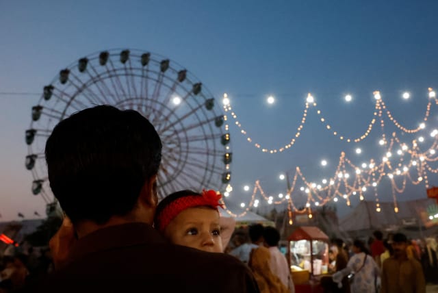  A man carries a baby while visiting a fair, during the second day of Eid al-Fitr celebrations, in Karachi, Pakistan April 11, 2024. (photo credit: REUTERS/AKHTAR SOOMRO)