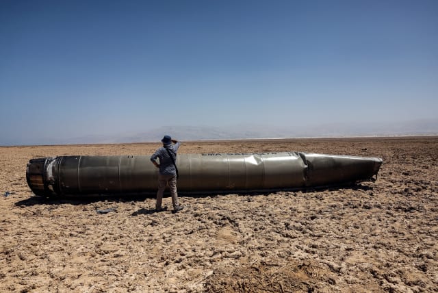  A man stands next to the apparent remains of a ballistic missile, as it lies in the desert near the Dead Sea, following a massive missile and drone attack by Iran on Israel, in southern Israel April 21, 2024  (photo credit: REUTERS/Ronen Zvulun)