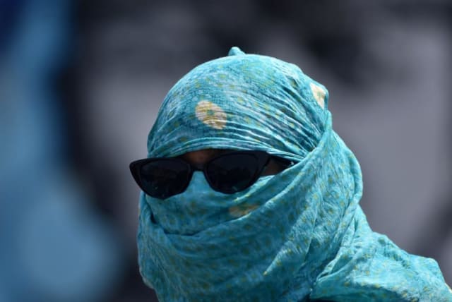  Una mujer lleva la cara cubierta con una bufanda para protegerse del calor en una carretera durante un caluroso día de verano en Bhubaneswar, India, 3 de mayo de 2024. (photo credit: STRINGER/ REUTERS)