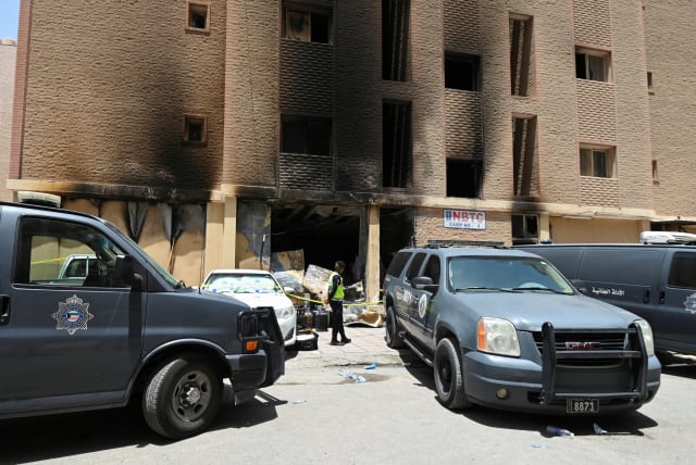 A Kuwaiti police officer is seen in front of a burnt building following a deadly fire, in Mangaf, southern Kuwait, June 12, 2024 (photo credit: REUTERS/STRINGER)