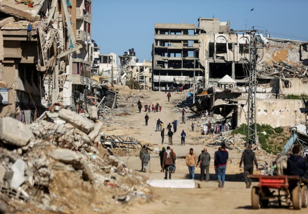  Palestinians walk past the ruins of houses destroyed in Gaza City, March 20, 2024