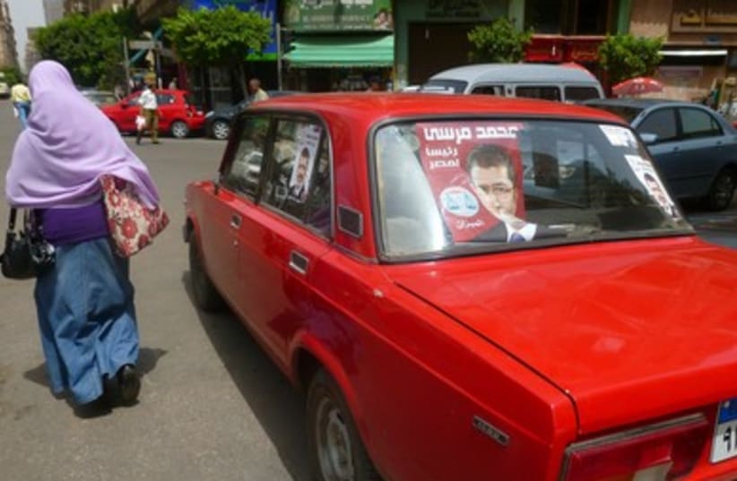 Woman walks by car sporting Mohamed Mursi posters