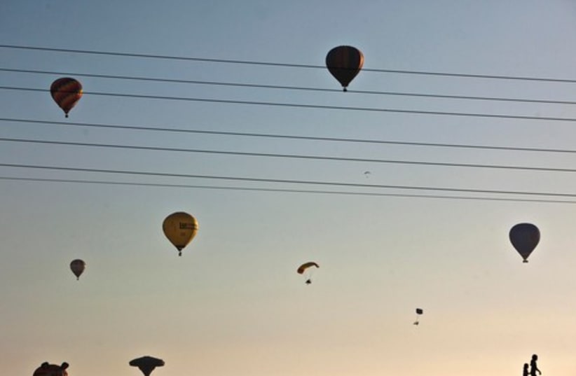 Children are silhouetted as hot air balloons and paragliders