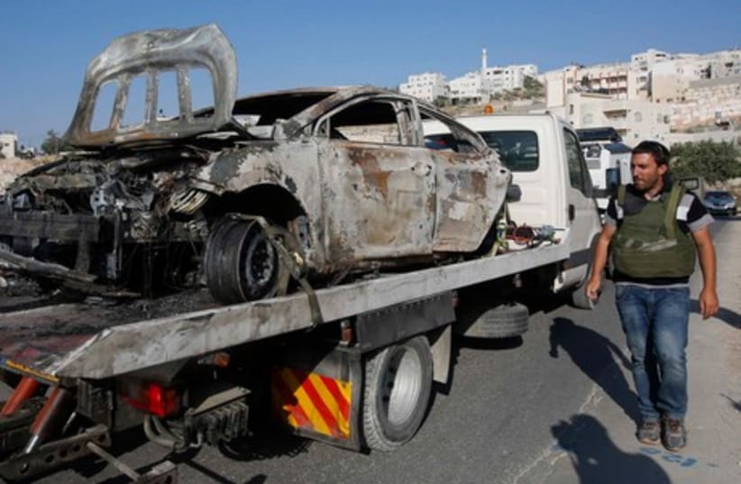An Israeli security officer walks next to a truck carrying a burnt car in the West Bank City of Hebron June 13, 2014.