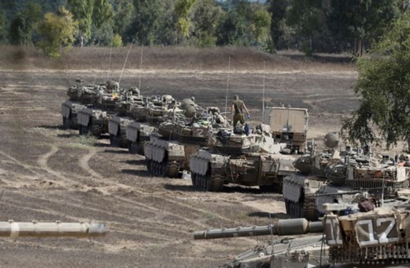 Israeli soldiers walk past tanks at a staging area near the border with Gaza Strip