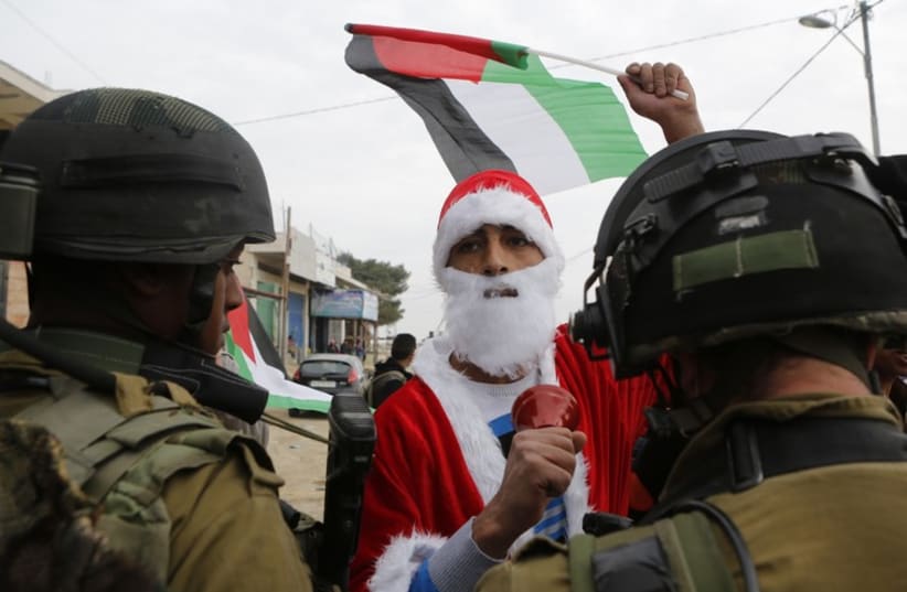 A Palestinian protester dressed as Santa Claus argues with an Israeli soldier during a demonstration against Israeli settlements near Bethlehem