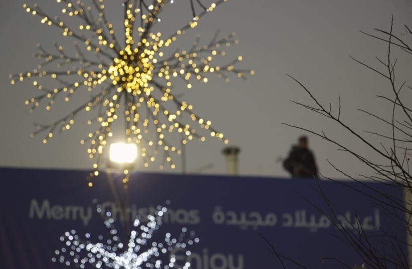 A security guard stands on a rooftop above a sign in Manger Square, Bethelehem, which reads ''Merry Christmas'' in English and ''A glorious Christmas'' in Arabic.