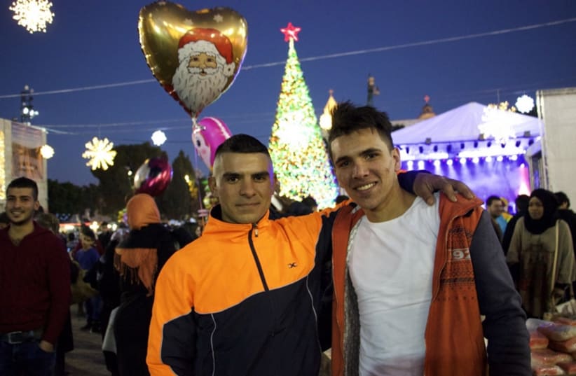 Two young men pose for a picture in Manger Square, Bethlehem, as a heart-shaped balloon with Santa Claus rises above them.