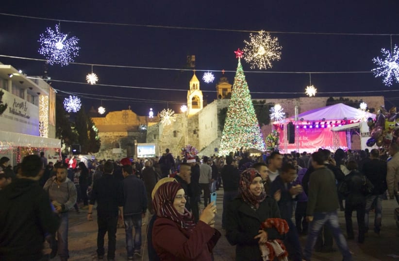  A large illuminated Christmas stands high over the crowd in Manger Square, Bethlehem on Christmas eve, which is buttressed by the the Church of Nativity and the Mosque of Omar.